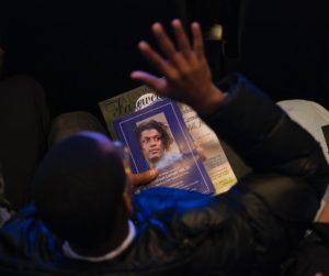 program for Deshaun Hill funeral service held by a man sitting with a hand raised.